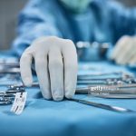 Surgeon picking up surgical tool from tray. Surgeon is preparing for surgery in operating room. He is in a hospital.