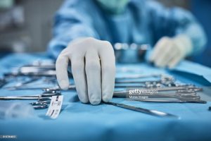 Surgeon picking up surgical tool from tray. Surgeon is preparing for surgery in operating room. He is in a hospital.